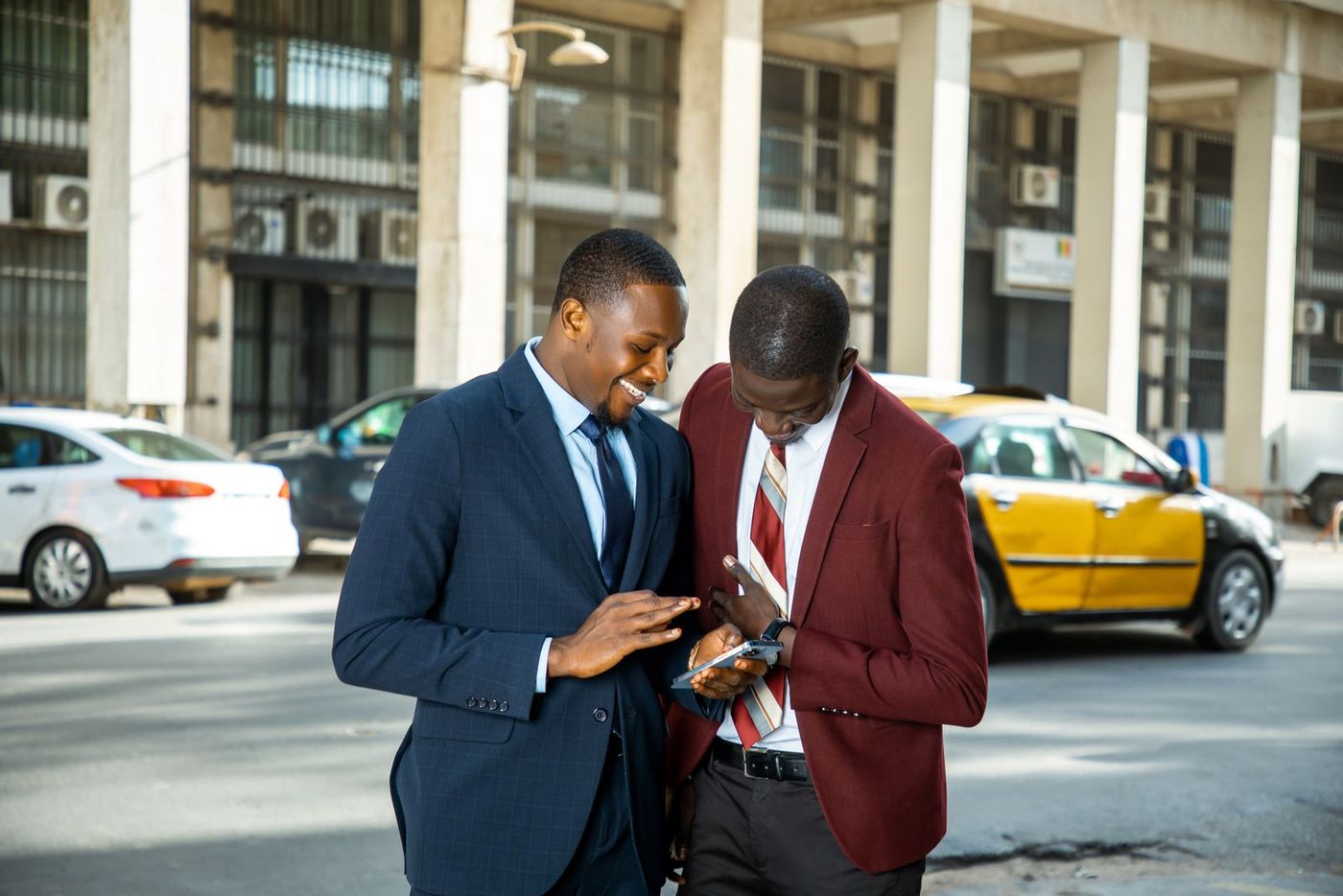 Two men in suits looking at a phone together on a street in Dakar