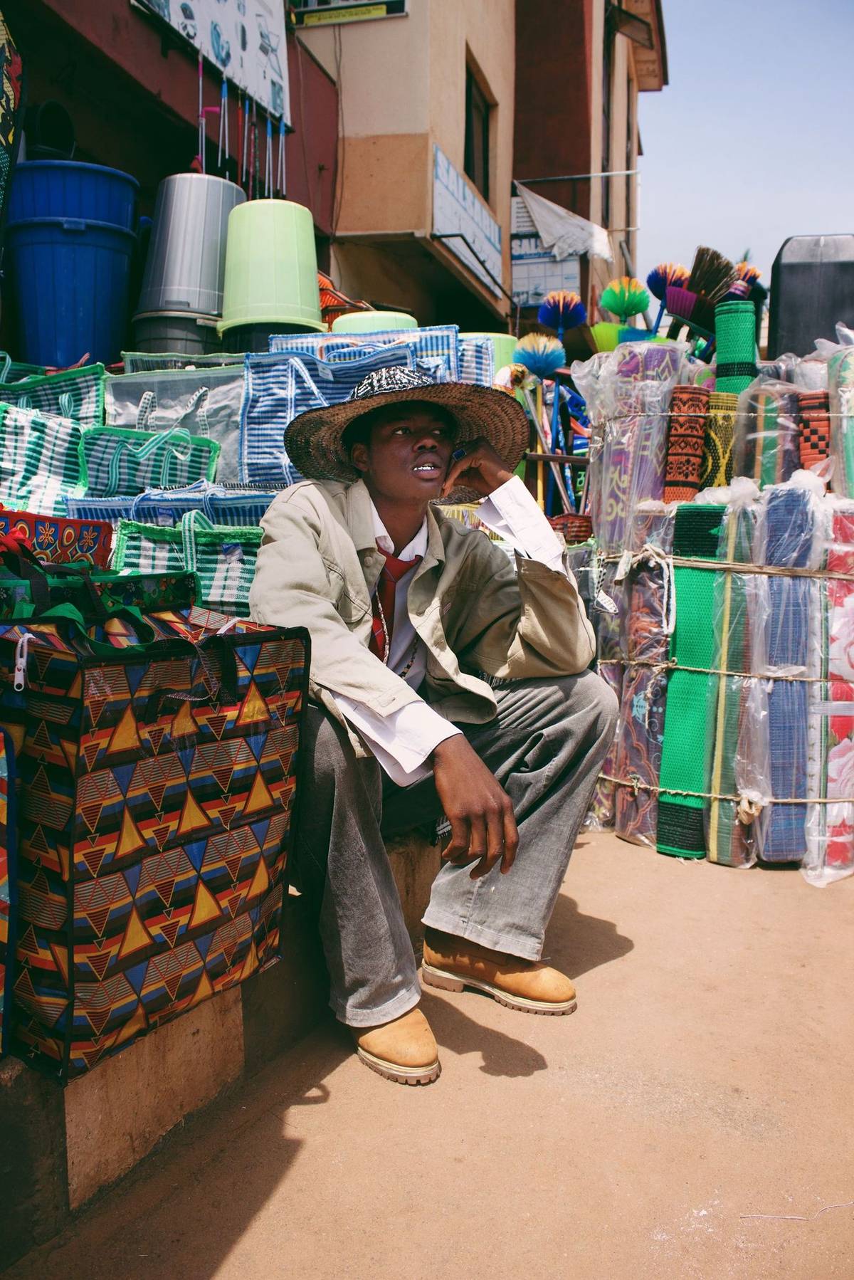 A young trader seated among woven bags and household goods at a market stall