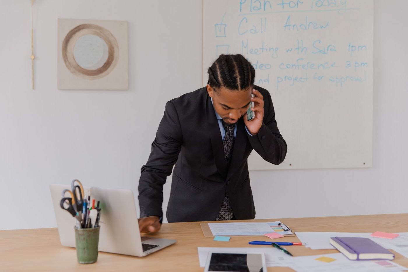 A man in a suit taking a call at a desk covered in printed documents