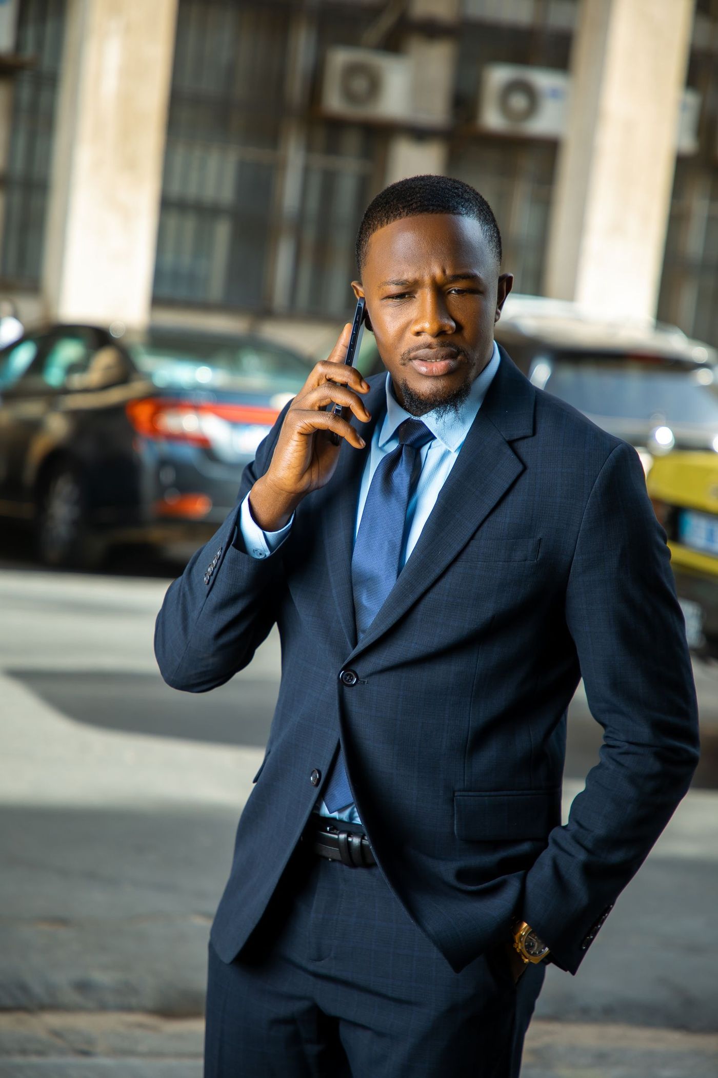A man in a navy suit taking a phone call on a city street